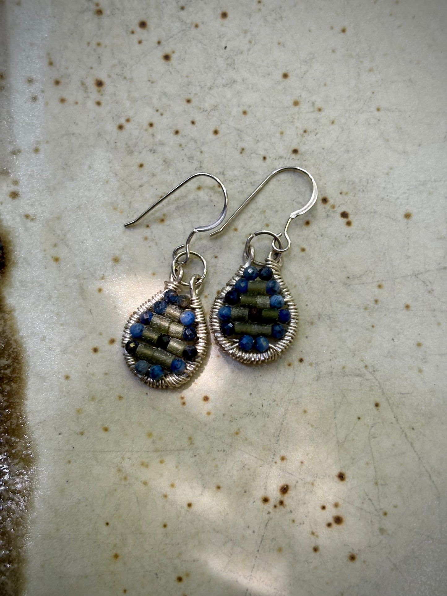 Pair of silver wire-wrapped earrings with garnet and jade stones on a textured surface