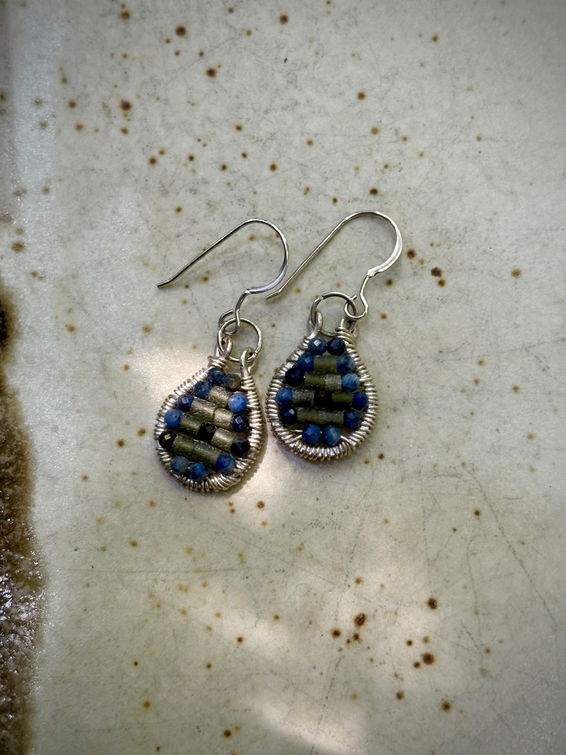 Pair of silver wire-wrapped earrings with garnet and jade stones on a textured surface