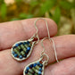Teardrop-shaped wire-wrapped earrings with jade and garnet stones on a hand against a blurred natural background
