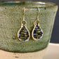 Teardrop-shaped wire-wrapped earrings with garnet and jade beads hanging on a textured ceramic cup.