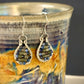 Pair of silver wire-wrapped earrings with garnet and jade stones on a ceramic mug with a colorful design.