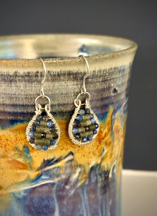 Pair of silver wire-wrapped earrings with garnet and jade stones on a ceramic mug with a colorful design.