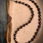 A close-up of a Freshwater Peacock Pearl Necklace with silver-plated S hook closure, featuring a variety of pearl colors such as copper, blue, purple, and green.